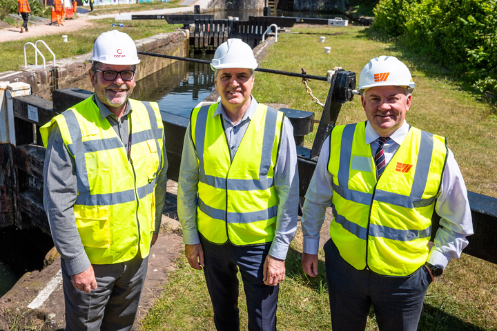 Photo of three people in high visibility jackets and hard hats stood in front of a canal